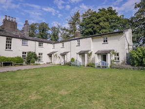 A traditional white building with multiple windows and doors, surrounded by a well-maintained lawn and trees. - The Gameskeepers Cottage (Grange-over-Sands)