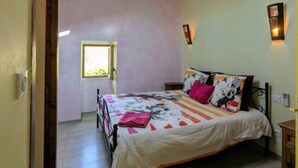 A bedroom with a skylight, a bed with a colorful bedspread, a nightstand, and a wooden floor.