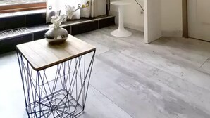 Una habitación moderna con una consola blanca, una pequeña mesa pedestal blanca, un adorno de pared y un televisor montado.