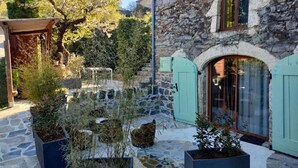 Un edificio de piedra con un patio cubierto, asientos exteriores y plantas en macetas.