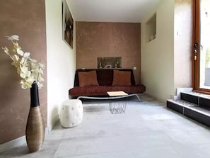 Ein modernes Wohnzimmer mit einem braunen Sofa, einem weißen Pouf, einer Vase mit weißen Blumen und einem gerahmten Bild an der Wand.