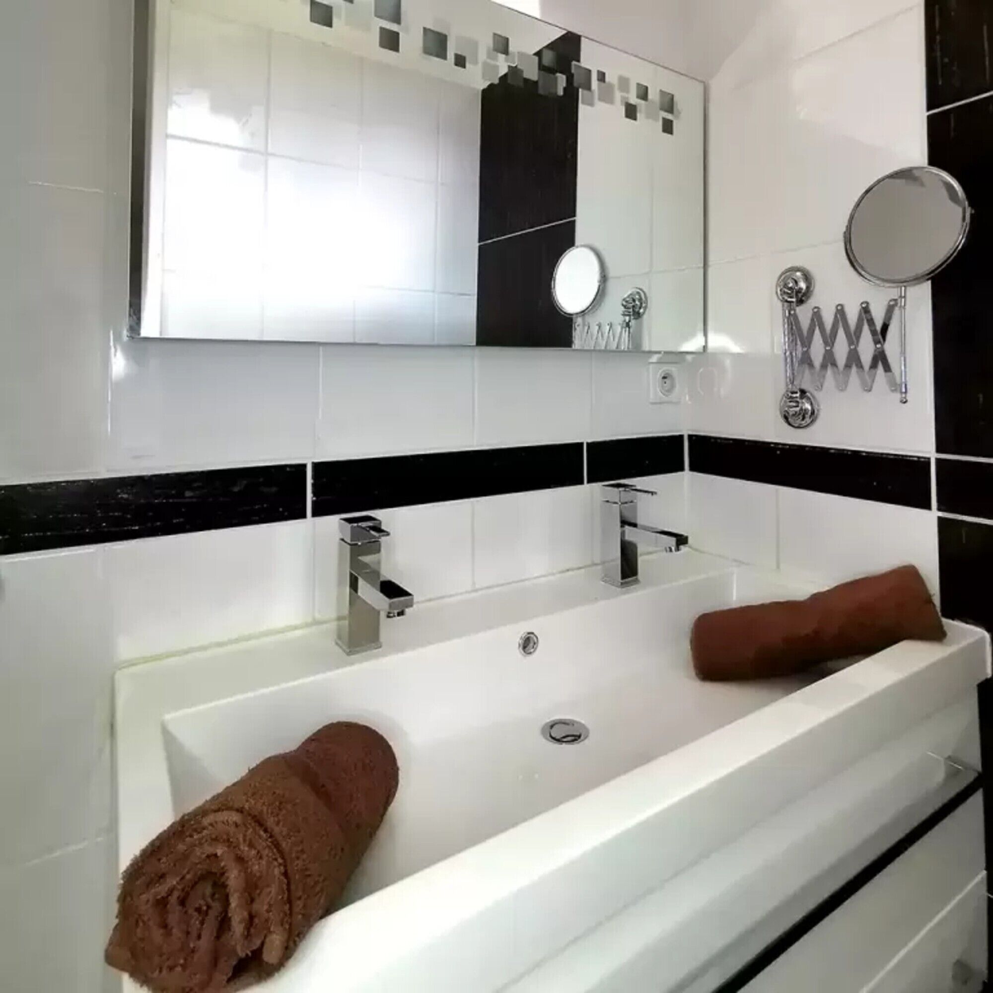 Um banheiro moderno com uma pia grande e branca, dois espelhos e um porta-toalhas.