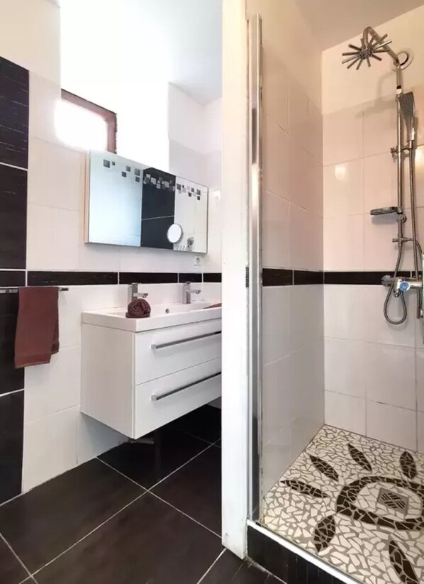 A bathroom with a shower, a sink with a mirror, and a towel hanging on the wall.