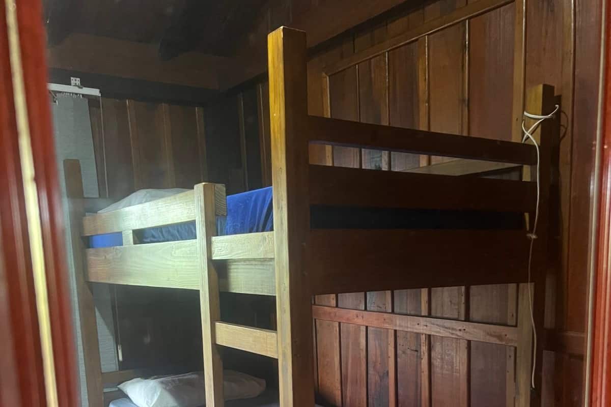Un lit superposé avec une structure en bois et une literie bleue, situé dans une pièce aux murs en bois et au sol carrelé.
