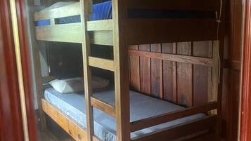 Una cama litera con estructura de madera y ropa de cama azul, ubicada en una habitación con paredes de madera y piso de baldosas.