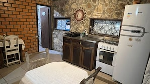 A kitchen with a stone wall, wooden ceiling, and a white refrigerator. - Villa Explorer (Imbituba)