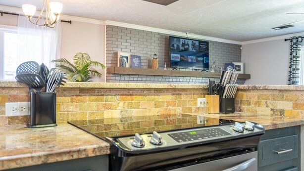 Een moderne keuken met een granieten aanrechtblad, een inbouwfornuis en een spatwand van kleurrijke tegels.