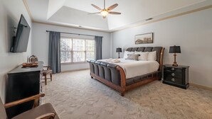 Un dormitorio con una cama grande, un ventilador de techo, un escritorio con silla, un televisor y una ventana con cortinas.