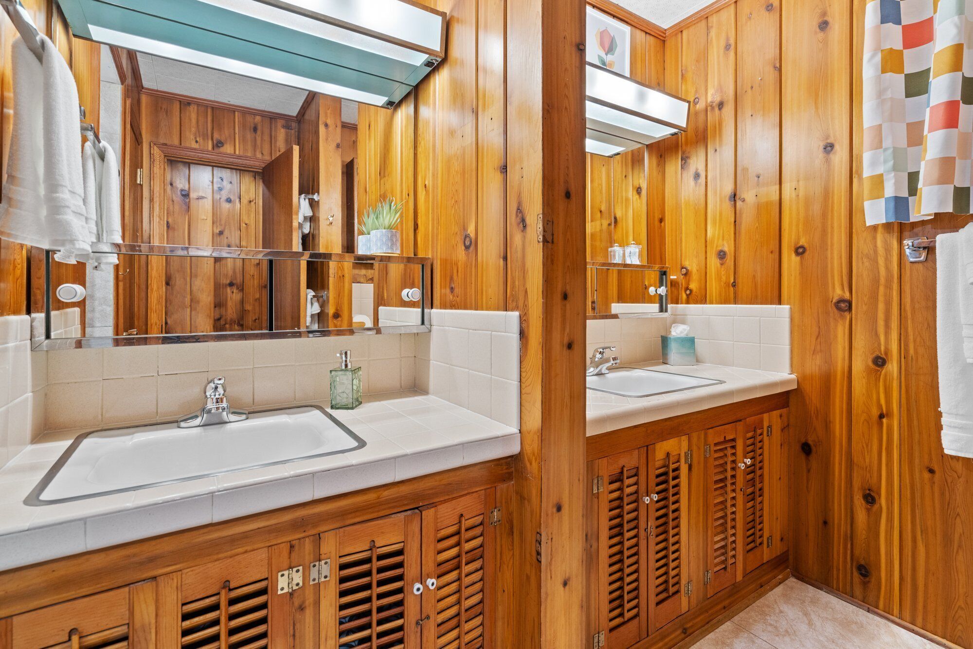 Un baño con paneles de madera, dos lavamanos, un espejo y una zona de ducha.