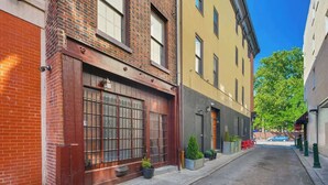 A narrow street with buildings on either side, featuring a brick facade and a yellow building with a door and windows. - Spacious Family-Friendly Home in Philadelphia (Philadelphia)