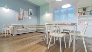 Una sala de estar con pared azul claro, un sofá gris, una mesa de comedor blanca con sillas y suelo de madera.