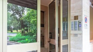 Entrada de hotel con puerta de vidrio, vistas a la vegetación exterior y un letrero de no estacionamiento en la pared.