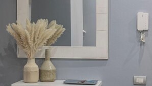 Un baño con un espejo, un tocador blanco, dos jarrones con plantas secas, un par de tijeras y un teléfono en la pared.