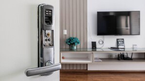 A modern door with a keycard reader, a wall-mounted TV, and a minimalist decor with a vase of flowers.