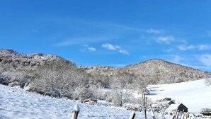 Un paysage enneigé sous un ciel bleu dégagé, avec une montagne en arrière-plan et un petit bâtiment au premier plan.