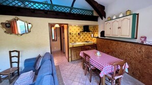Une pièce chaleureuse comprenant un canapé, une table à manger recouverte d’une nappe à carreaux, un coin cuisine avec des placards et un miroir décoratif.