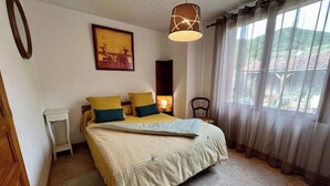 Une chambre à coucher avec un lit, une table de chevet, une lampe, une chaise et une fenêtre avec des rideaux.