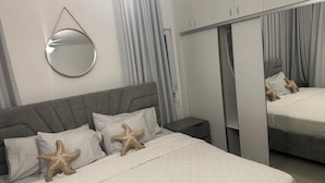 Ein Schlafzimmer mit Bett, Nachttisch, Kleiderschrank, Spiegel und Kissen mit Seesternen-Motiv.