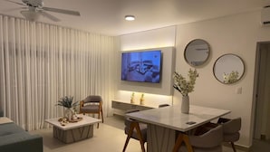 Ein modernes Wohnzimmer mit Flachbildfernseher, Esstisch mit Stühlen, einer Couch und einem Deckenventilator.