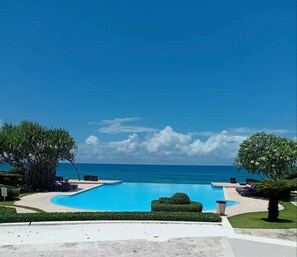 Ein Schwimmbecken mit Meerblick, umgeben von Grünpflanzen und Liegestühlen.
