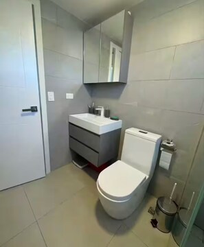 A modern bathroom with a white toilet, grey vanity, and a mirror above the sink. - Charming 1-bedroom apartment in enchanting Sosúa with AC, amazing restaurant (Sosúa)
