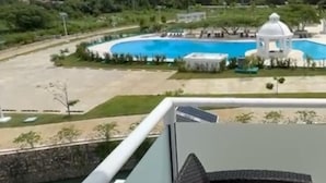 Ein Schwimmbad mit weißem Pavillon, umgeben von Grünpflanzen und blauem Himmel.