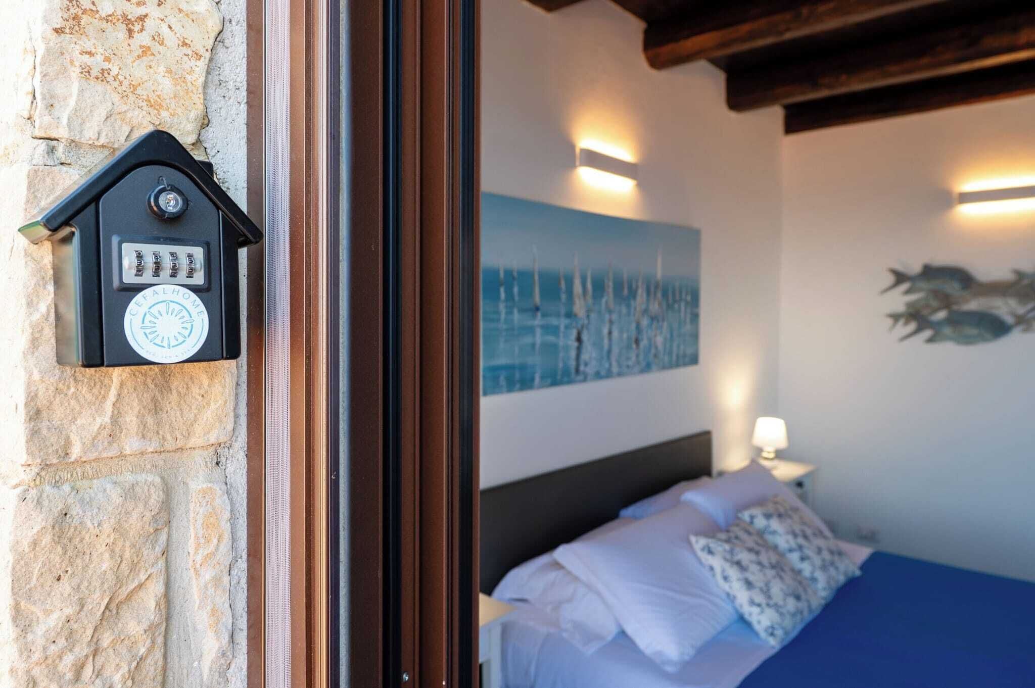 Ein Schlafzimmer mit Steinwand, einem Bett mit weißen und gemusterten Kissen, einem Segelbootgemälde und einer Wandleuchte.