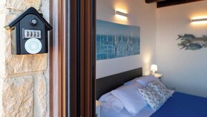 A bedroom with a stone wall, a bed with white and patterned pillows, a painting of sailboats, and a wall-mounted light fixture.