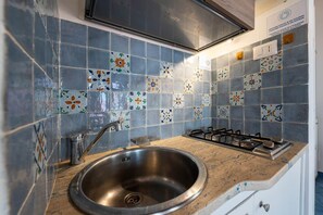 A kitchen with a stainless steel sink, a gas stove, and decorative blue and white tiles on the backsplash.