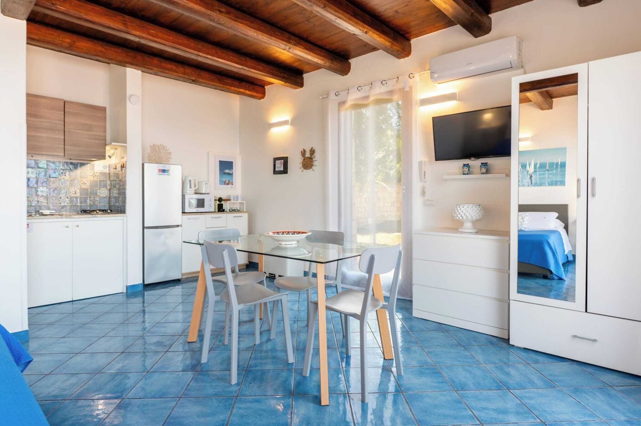 Una cucina compatta con mobili bianchi, un frigorifero, un forno a microonde e un tavolo da pranzo in vetro con sedie.