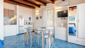 A compact kitchen with white cabinets, a refrigerator, a microwave, and a glass dining table with chairs.