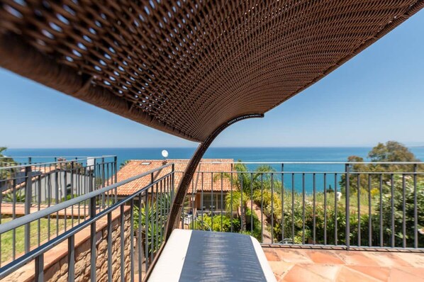 A balcony with a view of the sea, a metal railing, and a tiled roof.