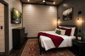 Een slaapkamer met een bed, nachtkastje, dressoir, schilderij en plafondventilator.