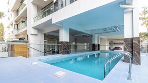Ein moderner, überdachter Pool mit klarem, blauem Wasser, umgeben von einer gefliesten Sonnenterrasse und Glasgeländern.