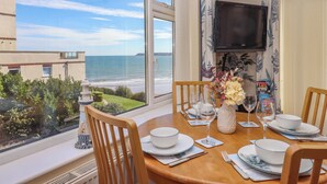 A dining area with a view of the sea, a television, and a table set for four. - Beachside (Paignton)