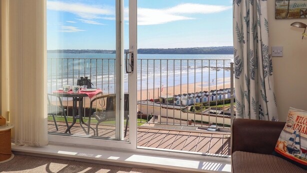 A balcony with a view of a beach and sea, a table with chairs, and a couch. - Beachside (Paignton)