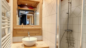 Ein Badezimmer mit einem Holzkosmetikschrank, einem weißen Waschbecken, einem Spiegel und einer Duschkabine.