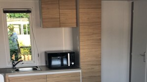 A compact kitchen with wooden cabinets, a microwave, a sink, and a dining table with white chairs.