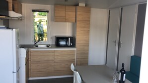 A compact kitchen with a microwave, wooden cabinets, a sink, and a window with a view of greenery.