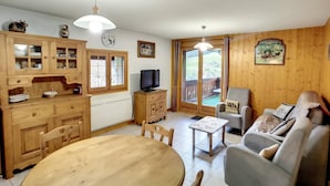 Ein gemütliches Zimmer mit Holzkästen, einem Esstisch, einer Couch und einem Fernseher.