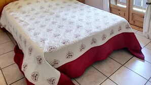 Ein Schlafzimmer mit einem hölzernen Kopfteil, einem Bett mit einem gemusterten Bettbezug, einer Nachttischlampe und einem Fenster mit Vorhängen.