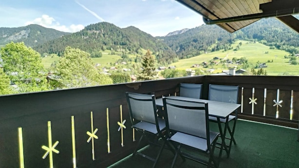 Ein Balkon mit Tisch und Stühlen mit Blick auf eine gebirgige Landschaft.