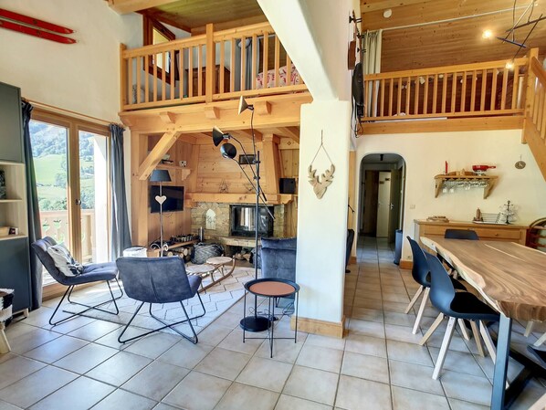 A spacious living area with a wooden staircase, a fireplace, and a dining area with modern furniture.