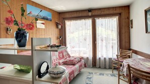 Une pièce chaleureuse avec un décor intérieur en bois, un lit avec une literie à motifs, une table à manger avec des chaises et une grande fenêtre avec des rideaux.