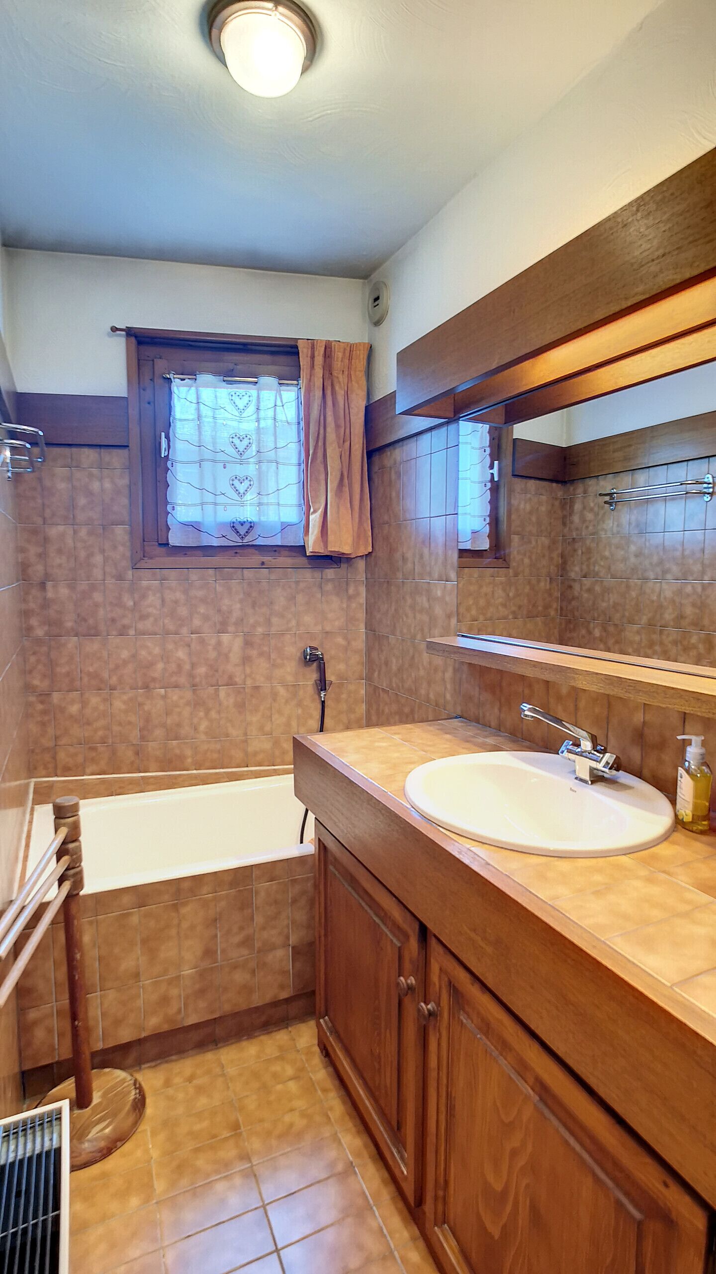 Un baño con bañera, lavabo, ventana con cortina y espejo sobre el lavabo.