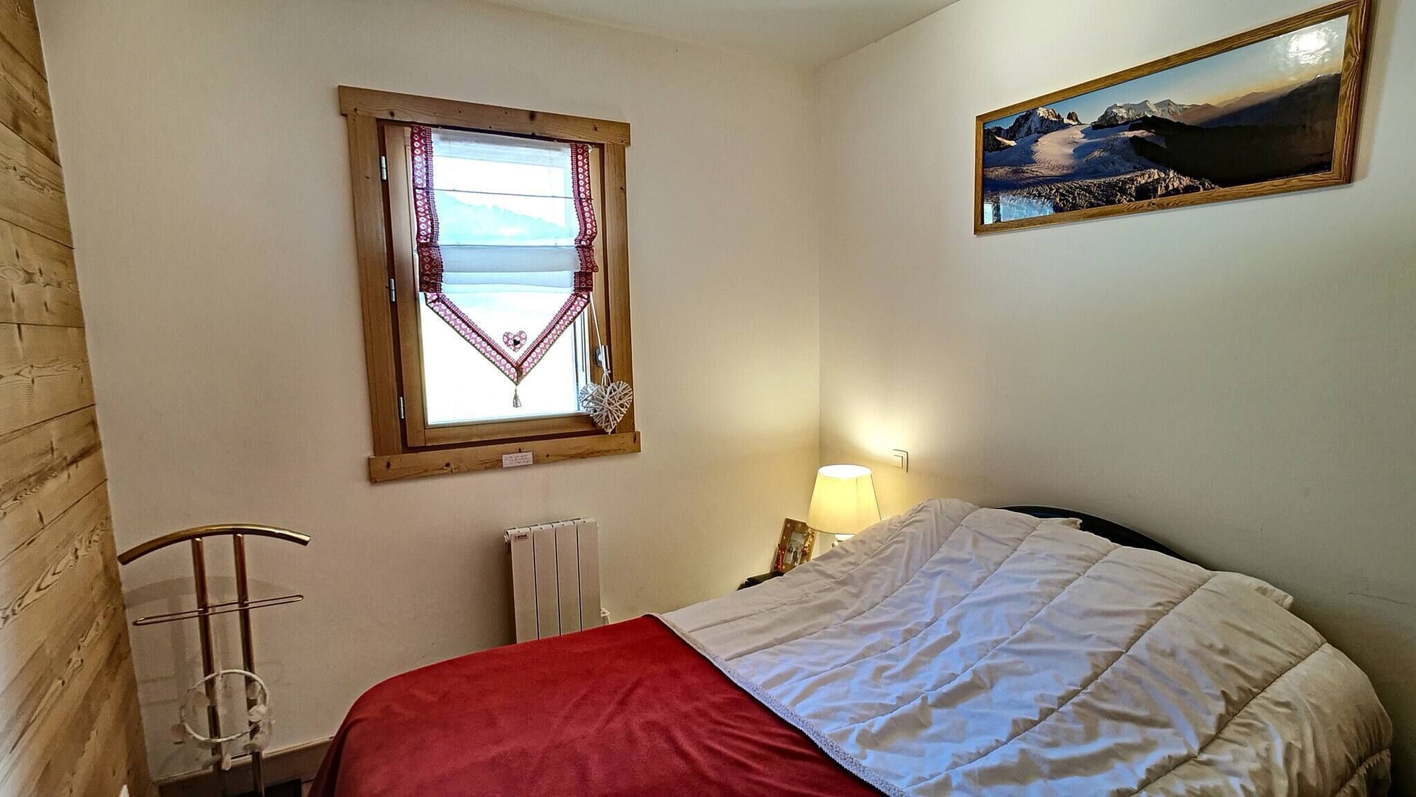 Un dormitorio con cama, ventana con vistas, un cuadro en la pared y un radiador.