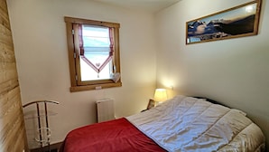 Une chambre à coucher avec un lit, une fenêtre donnant sur un beau paysage, un tableau au mur et un radiateur.