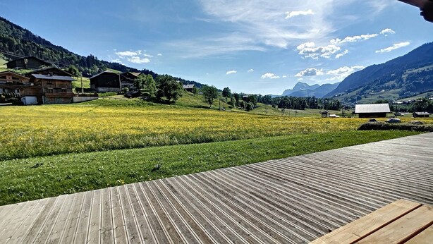 Une terrasse en bois donnant sur un paysage rural, avec des champs et des maisons.
