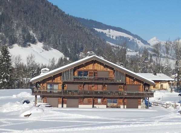 A wooden chalet with a balcony, surrounded by snow-covered mountains.