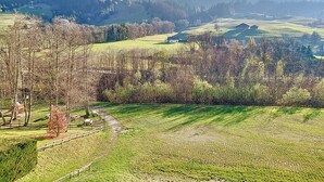 Vista de uma paisagem rural com colinas ondulantes, uma casa pequena e um parquinho.